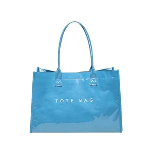 Detalle del bolso tote de PVC azul brillante con estampado 'TOTE BAG' y asas superiores.