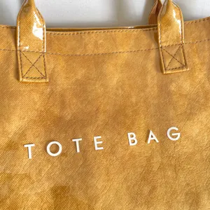 Primer plano detallado de un bolso tote de PVC amarillo texturizado con letras.