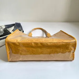Vista detallada de un bolso tote amarillo con capa exterior de PVC transparente.