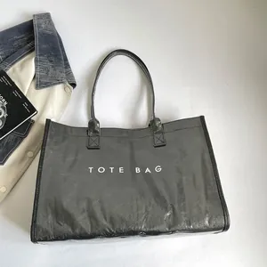 Detalle de un bolso tote de PVC gris brillante con la inscripción TOTE BAG en color blanco