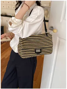 Mujer a la moda que lleva un bolso de hombro informal de paja tejida a rayas negras y beige.