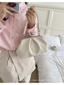 Elegant cream-colored pleated cloud bag with vintage metal frame held by a model