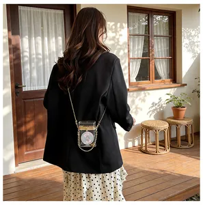 Back view of a woman styling a transparent acrylic box bag with a gold beaded chain