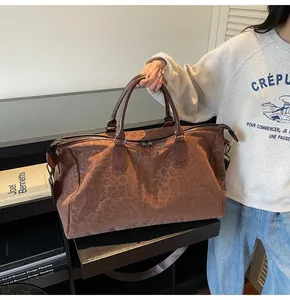 Large leopard print duffle bag held by a model in a stylish indoor lifestyle setting.