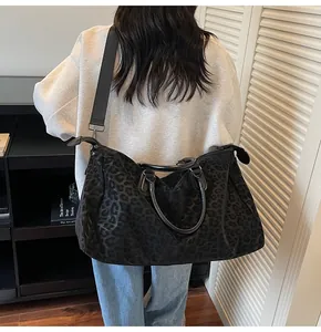 Detail view of a large black leopard print travel bag worn as a shoulder bag.