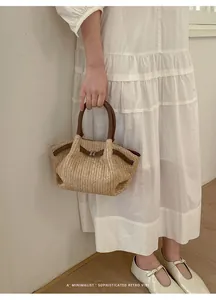 Modelo con un bolso de paja tejida con asas de cuero marrón en un vestido blanco.