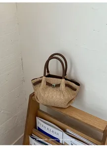 Vista detallada de un bolso de paja trenzada con asas de cuero marrón sobre madera