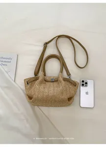 Bolso de mano de paja tejida de verano con correas de cuero junto a un teléfono inteligente