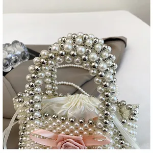 Dettaglio ravvicinato di borsa a secchiello in perle bianche e argento con fiocco rosa