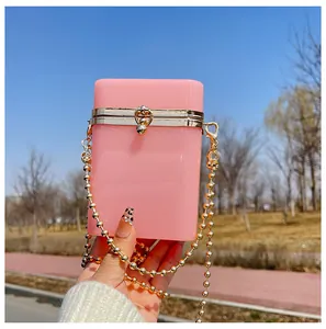 Close-up detail of a pink acrylic box clutch bag featuring a gold bead chain strap in natural light.