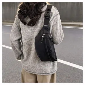 Rear view of a minimalist black sling bag worn over a casual grey knit sweater outdoors