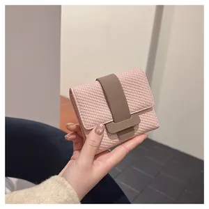 Pink textured tri-fold women's wallet with brown strap held in hand showing the scale
