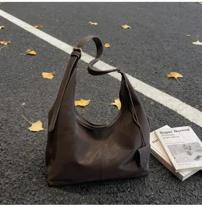 Dark brown minimalist hobo bag detail shot with autumn leaves on asphalt background