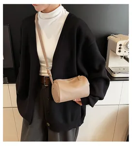 Minimalist tan PU leather cylinder pillow bag worn by a model in a black cardigan