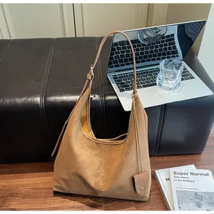 Minimalist tan hobo shoulder bag styled with laptop and books in a modern setting