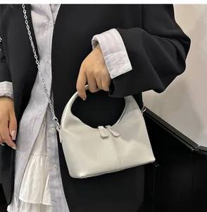 Close-up of a minimalist white soft PU handbag held by a model in a black blazer