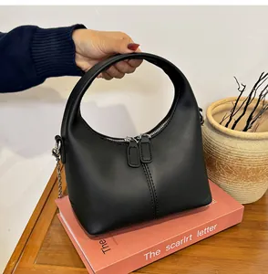 Detailed view of a chic black soft PU leather handbag held and placed on a pink book.