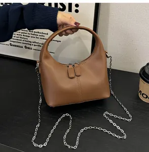 Detail view of brown PU leather handbag with circular handle and silver chain strap.