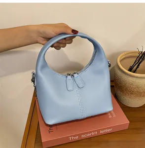 Close-up of a light blue soft PU leather handbag with dual zippers on a vintage book.