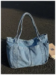Bolso tote de mezclilla azul con múltiples bolsillos en suelo exterior con textura y libros