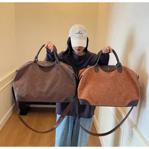 Asian model holding brown and camel tan suede retro travel duffle bags in a hallway
