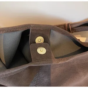 Close-up detail of the durable golden magnetic snap closure on a brown suede shoulder bag