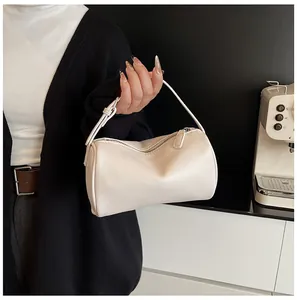 Detailed view of a minimalist cream PU leather pillow bag held by a model.
