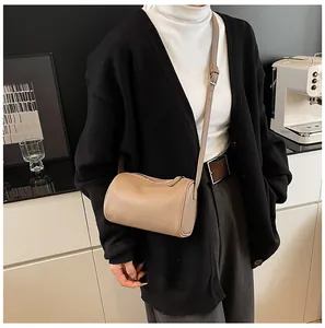Minimalist beige textured PU leather barrel pillow bag shown worn as a crossbody accessory