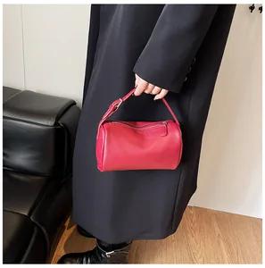 Detailed view of a red pebble grain PU leather pillow bag held by model in black coat