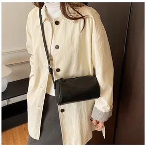 Minimalist black PU leather cylindrical pillow bag styled with a stylish cream jacket