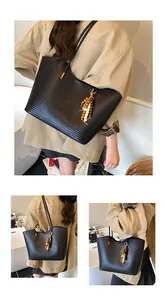 Detail view of a stylish black woven underarm tote bag with a decorative wooden bead charm