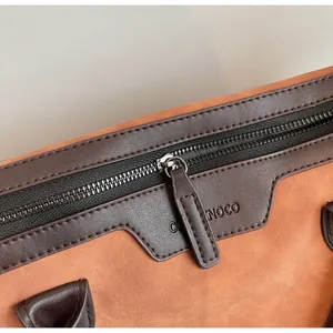 Close-up detail of smooth metal zipper and debossed logo on a two-tone leather tote bag