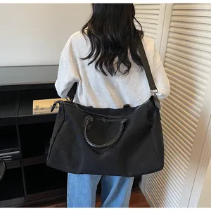 Grand sac de voyage noir imperméable en nylon porté à l'épaule dans un cadre de vie