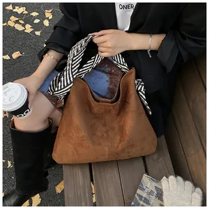 Vintage brown suede tote bag with striped scarf handle in an autumn setting.