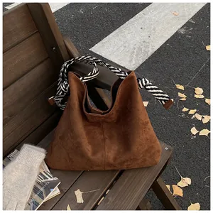 Detail of a vintage brown suede hobo bag with a braided rope handle on a wooden bench.