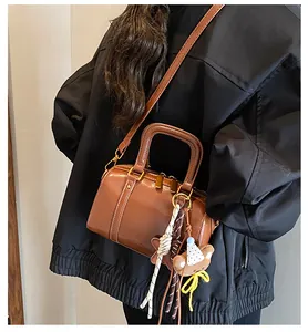 Minimalist brown Boston bag with cute bear charm and shoulder strap detail.