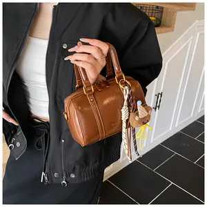 Stylish brown mini Boston handbag with decorative bear charm shown in a close-up view.