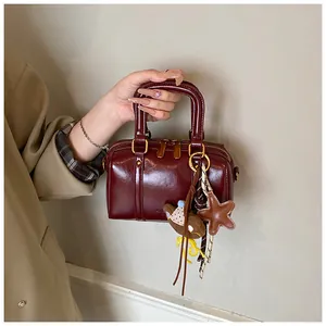 Close-up of a glossy burgundy mini Boston bag with decorative charms held by a person.