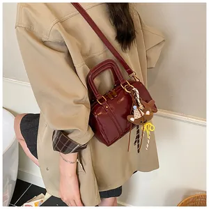 Detail of a glossy burgundy Boston bag worn crossbody with a cute teddy bear charm.