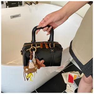 Detailed view of a sleek black Boston handbag held by hand featuring cute bear charms