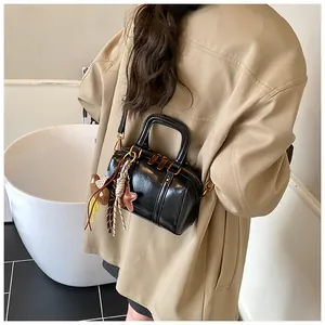 Detail view of a stylish black Boston handbag with decorative charms worn by a model.