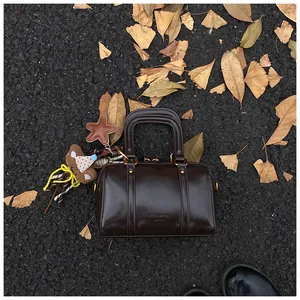 Macro view of a glossy brown Boston bag with a cute teddy bear charm on leaves