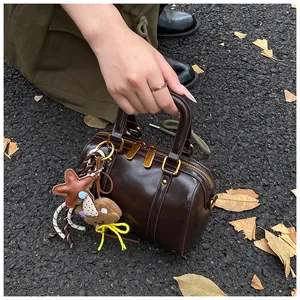 Close-up of a brown double-zipper Boston handbag held by a person in an outdoor setting