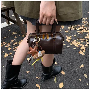 Minimalist coffee brown dual-zip Boston handbag carried by a model on an autumn path.