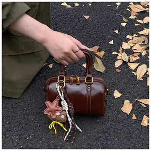 Chic brown glossy Boston bag with cute star and cookie charms on autumn street