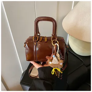 Detail of a glossy brown Boston bag with dual zippers and a cute bear charm.