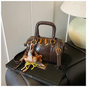 Detail view of a brown mini Boston handbag with a cute bear charm on a dark surface