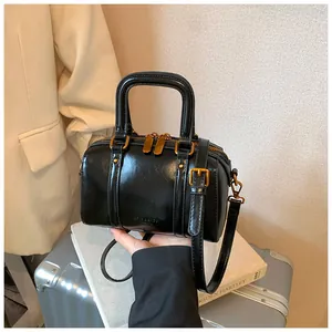 Handheld view of a chic black Boston bag with shiny leather and gold hardware.