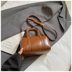 Detail view of a brown glossy Boston handbag styled on a grey blazer with handle