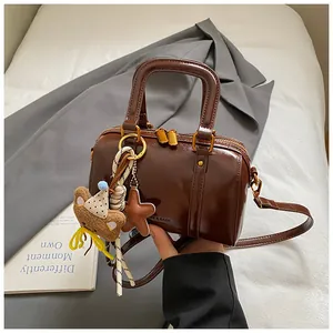 Detailed close-up of a brown glossy Boston bag featuring a cute teddy bear charm